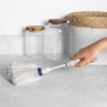 White duster with blue handle being used to clean kitchen worktop