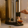 Hot water urn dispensing tea into a glass cup, silver colour, countertop use
