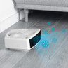 White portable fan heater placed on grey laminate floor under sofa, showing cool air function.