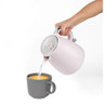 Person pouring hot water from pale pink electric kettle into grey mug, product in use