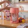 Electric blender with ice being added, surrounded by juice cartons and fresh fruit