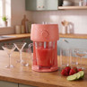 Red slushie maker with jug on kitchen counter, strawberries and lime beside glasses