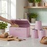 Pink bread bin with matching labelled canisters on kitchen counter, sliced bread visible