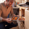 Person removing tray of roasted potatoes and vegetables from oven in home kitchen.