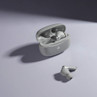 Grey wireless earbuds in open charging case, with one earbud placed outside on a light background