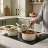 Cream saucepan set on hob with stew, being stirred, in modern kitchen setting