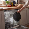 Hand removing black dishwasher cover from clean plates in modern kitchen.