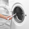 Hand using cleaning brush on washing machine drum for targeted cleaning demonstration