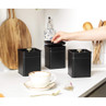 Set of three matte black kitchen storage tins, one with lid open on worktop