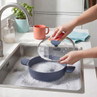 Blue silicone pan and lid being washed in sink, shown with sponge