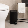 Black pedal bin in bathroom, shown beside toilet and towel rack.