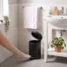 Black pedal bin with lid open beside bathroom sink, shown in use