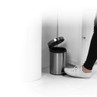 Silver pedal bin with open lid shown in bathroom, foot pressing pedal