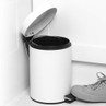 White pedal bin with open lid, shown in corner of a room with trainer pressing pedal