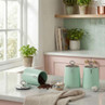 Set of three mint green kitchen canisters for sugar, coffee, and tea on counter.