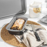 Non-stick silver loaf tin with baked strudel, knife and tea towel on kitchen counter