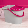Grey mop bucket with pink wringer and handle on pale wooden flooring
