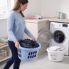 Woman carrying blue laundry basket beside open washing machine