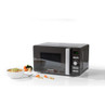 Black microwave oven with open door, bowl of soup inside, carrots and broccoli on side