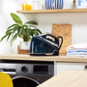 Steam generator iron in navy and cream on laundry room worktop next to folded shirts.