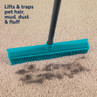 Teal rubber broom sweeping pet hair from beige carpet, demonstrates cleaning effectiveness