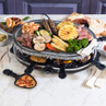 Electric raclette grill with granite hot stone, shown cooking mixed meats, seafood, and vegetables