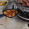 Raclette grill with melting cheese and chorizo in tray, beef and aubergine grilling on top
