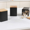 Set of black kitchen storage canisters with wooden lids, one open showing teabags.