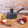 Black non-stick saucepan with glass lid on kitchen counter, shown with potatoes, onion, and pepper.