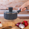Black speckled saucepan with lid held by hand, shown in a modern kitchen.