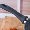 Speckled black non-stick frying pan handle close-up on wooden surface
