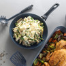 Non-stick frying pan with penne pasta, green vegetables and cheese, next to roast chicken and veg