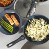 Non-stick frying pans with salmon, asparagus, and creamy pasta, shown from above.