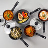 Set of five black non-stick saucepans with lids, shown with assorted cooked food.
