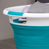 Collapsible turquoise laundry basket with clothes inside, shown on a wooden floor