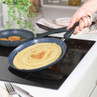 Crepe in non-stick frying pan on induction hob, hand holding handle