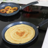 Two non-stick frying pans on induction hob, one with a pancake, one with cooked apple rings.