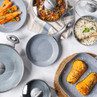 Set of grey non-stick frying pans and pots with food, shown on kitchen surface