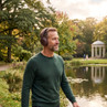 Man in green jumper wearing brown wireless headphones outdoors by a lake