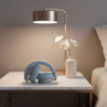 Foldable blue wireless headphones on bedside table with lamp and white orchid vase