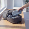 Blue portable speaker being packed in a grey travel bag on a wooden table