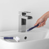 Person cleaning chrome tap with blue and white cleaning brush over white bathroom sink