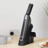 Black cordless handheld vacuum cleaner in charging base on a light wood desk