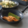 Non-stick frying pan with cooked salmon fillets and asparagus, shown on a kitchen worktop.