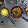 Set of blue non-stick saucepans with glass lids, shown cooking rice and curry, on kitchen surface