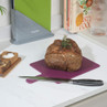 Roast beef joint on purple chopping board with knife, salt and pepper pots nearby.