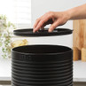 Black metal bread bin with lid, hand lifting top in modern kitchen