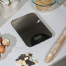 Silver digital kitchen scale on white worktop, with eggs, flour, and rolling pin nearby