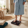 Person in blue bathrobe standing on black digital bathroom scale in modern bathroom