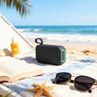 Portable black Bluetooth speaker on beach towel near sunglasses and sun lotion